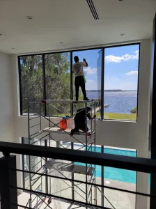 High-access residential window tinting installation on large floor-to-ceiling windows overlooking a lake.